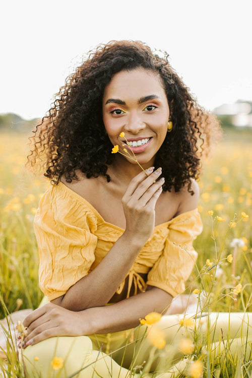 Femme souriante assise dans un champ fleuri et tenant des feuilles jaunes. 