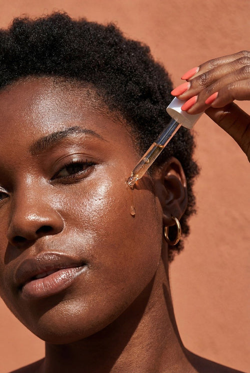Une femme à la peau éclatante applique du sérum sur son visage avec un compte-gouttes.