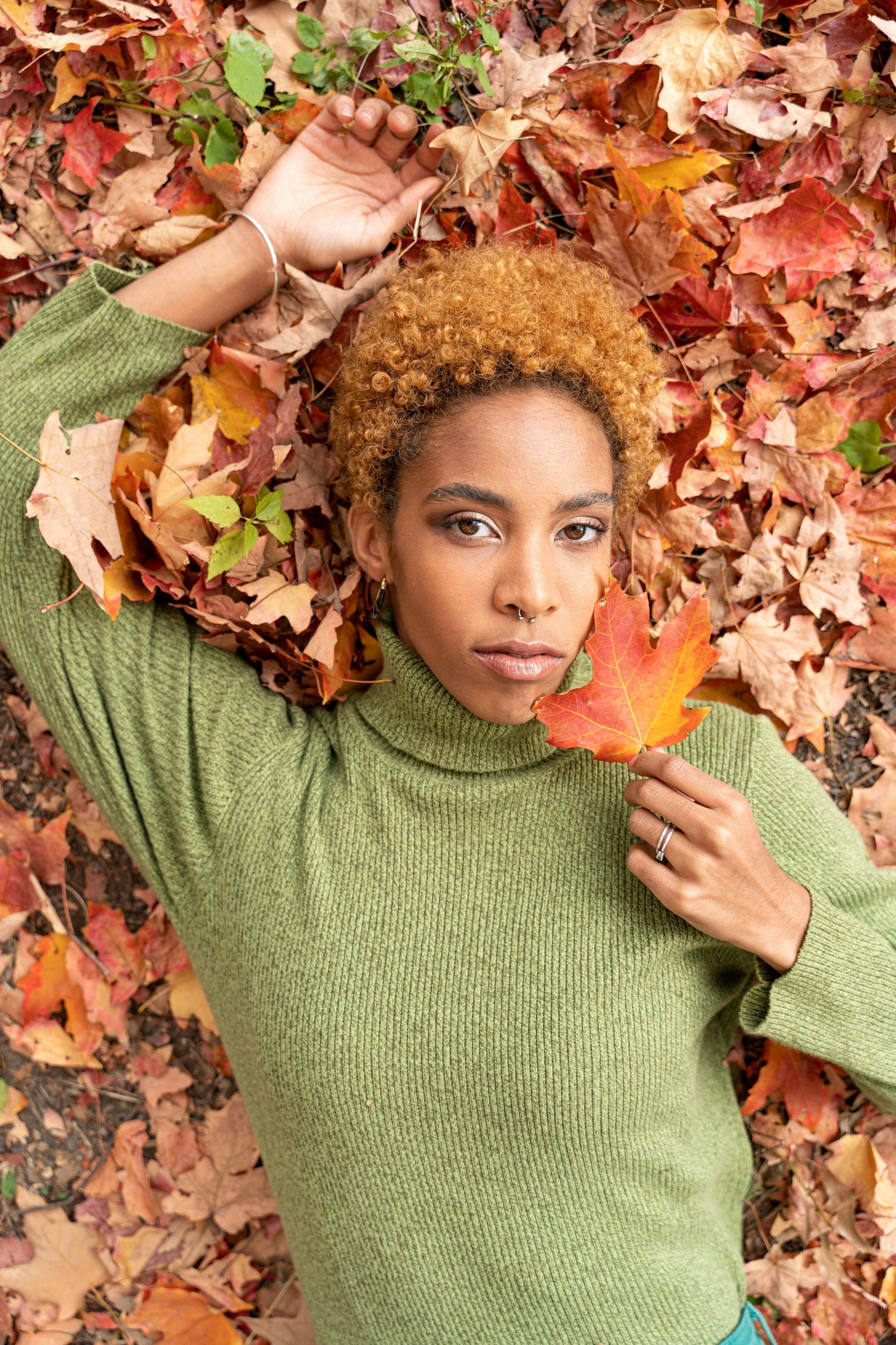Fille allongée par terre, en col roulé vert et tenant une feuille d’érable jaune et rouge.