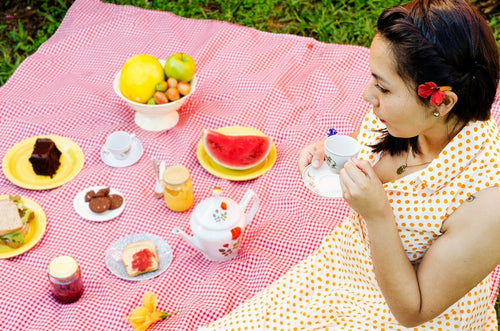 Femme assise sur une nappe de pique nique tenant une tasse de café.