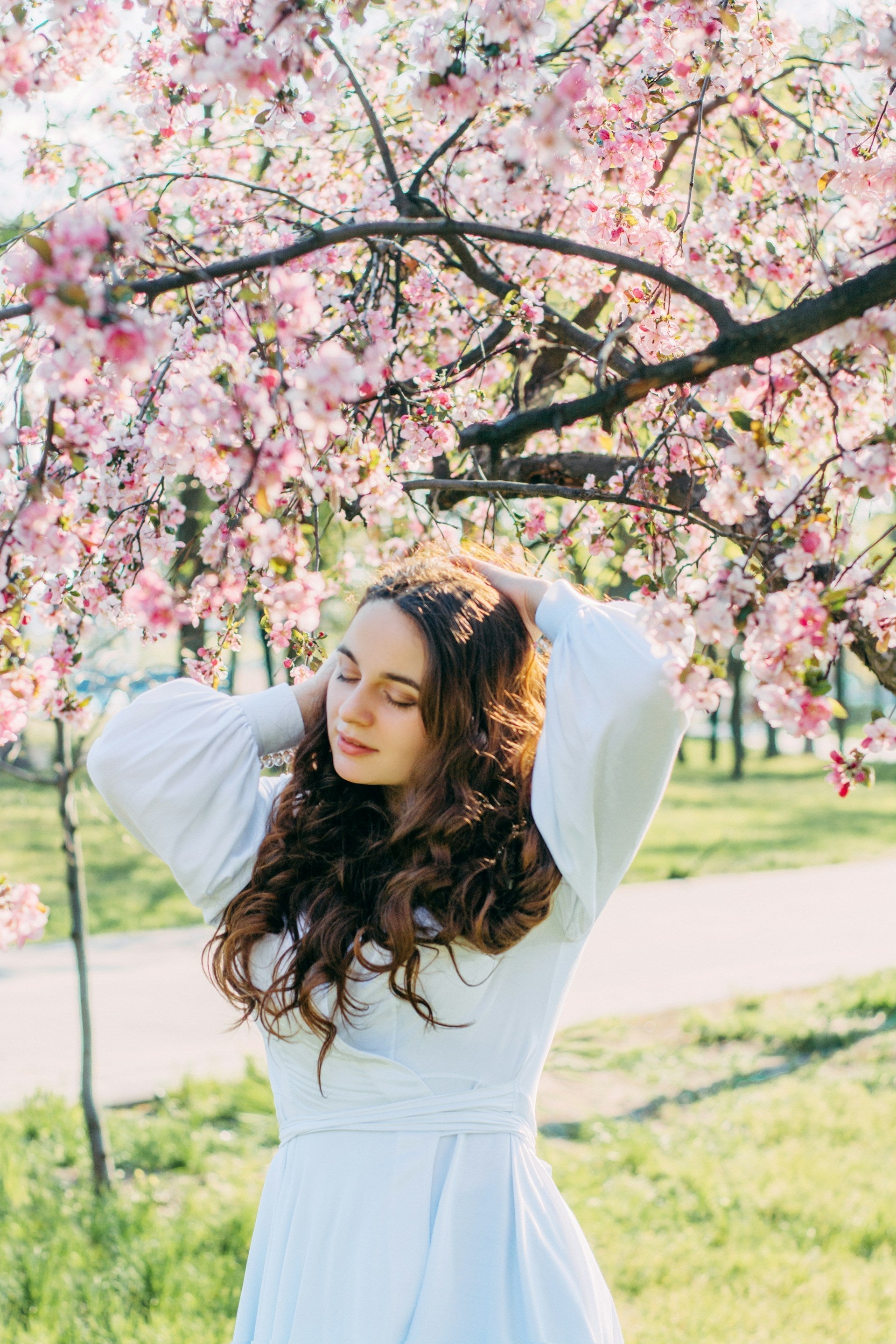  Femme en robe blanche à chemises longues sous un arbre composé de fleurs de cerisier.