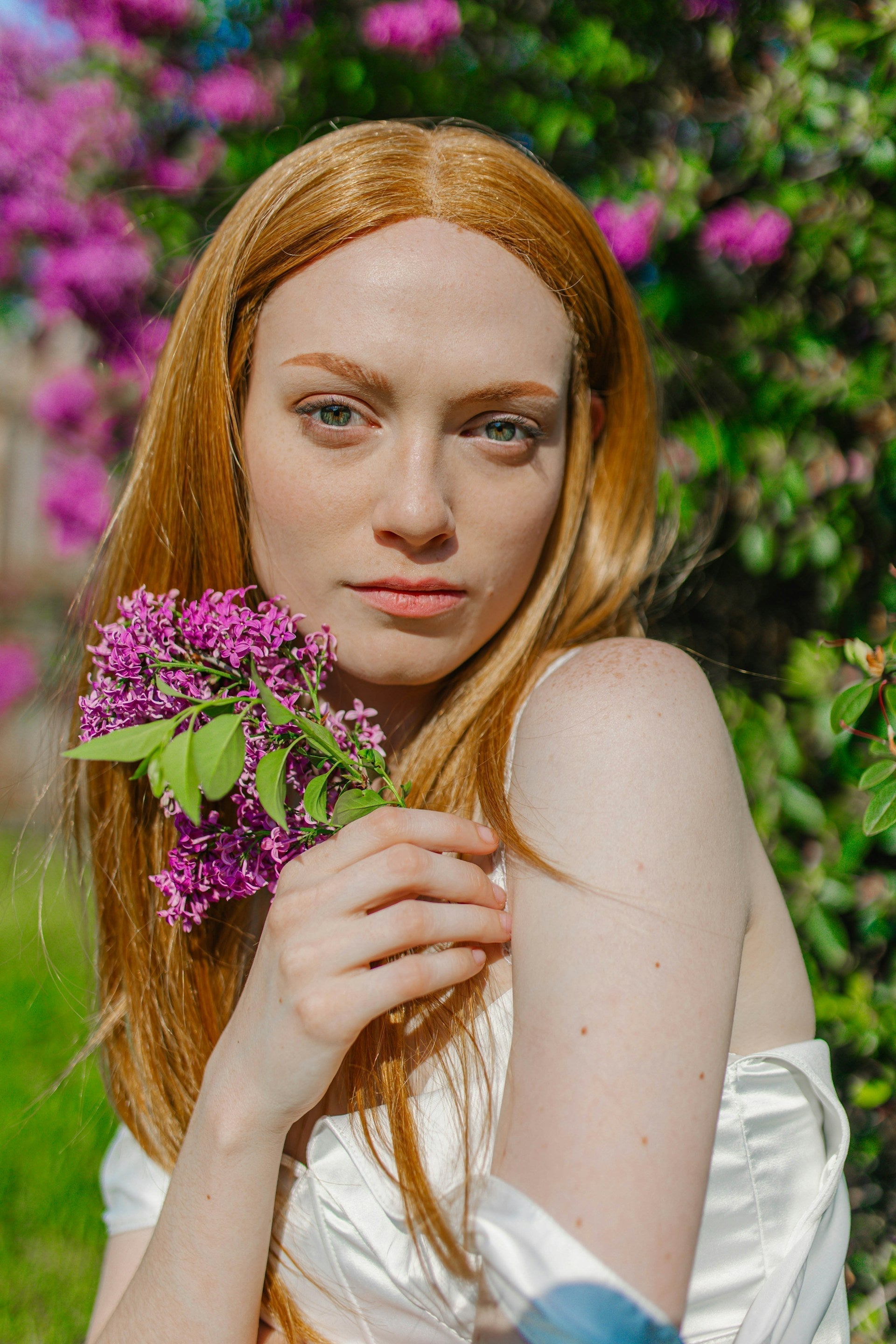 Portrait d’une femme en robe blanche dans un décor fleuri tenant une fleur violette.