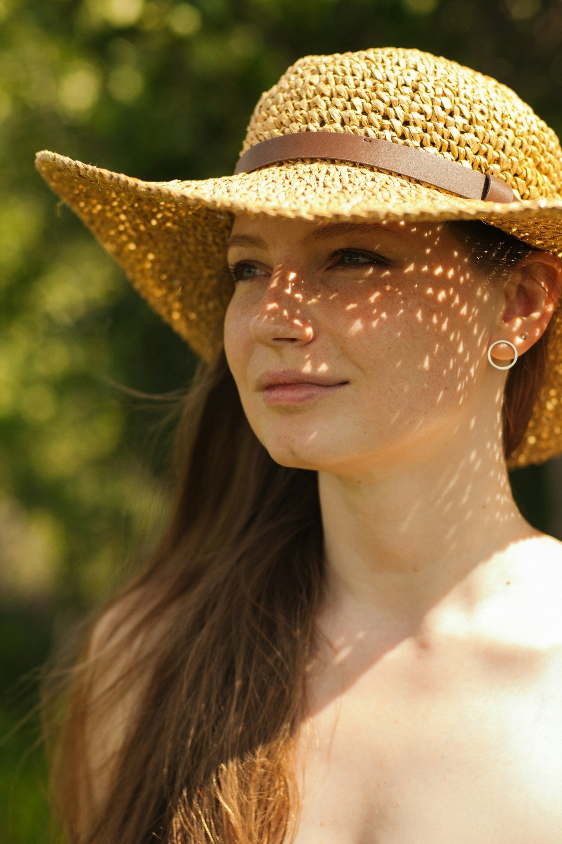 Portrait d’une femme avec un chapeau de soleil beige, les épaules dénudées. 